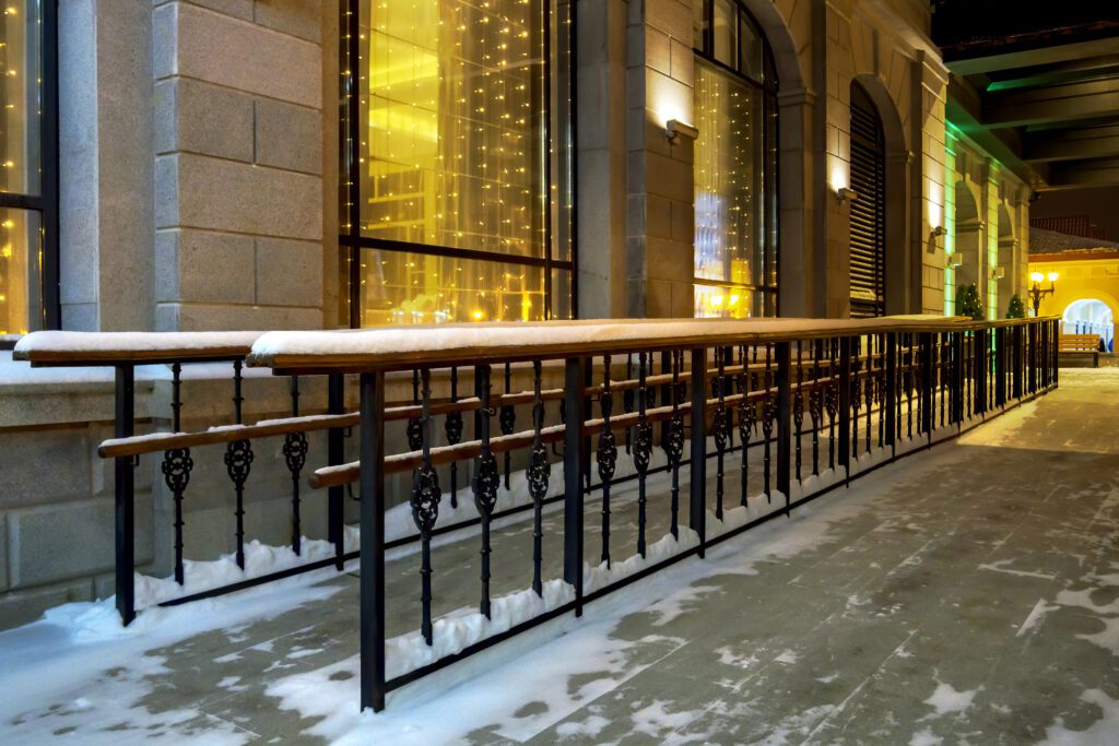 Concrete ramp with wooden handrails that runs along the side of  building to the entrance. The setting is  a wintry night.